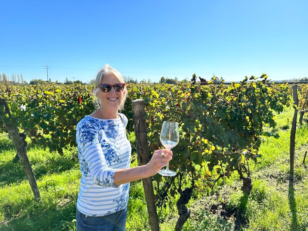 Susan Richards of Always Sharing Wine holding a glass in a vineyard and smiling
