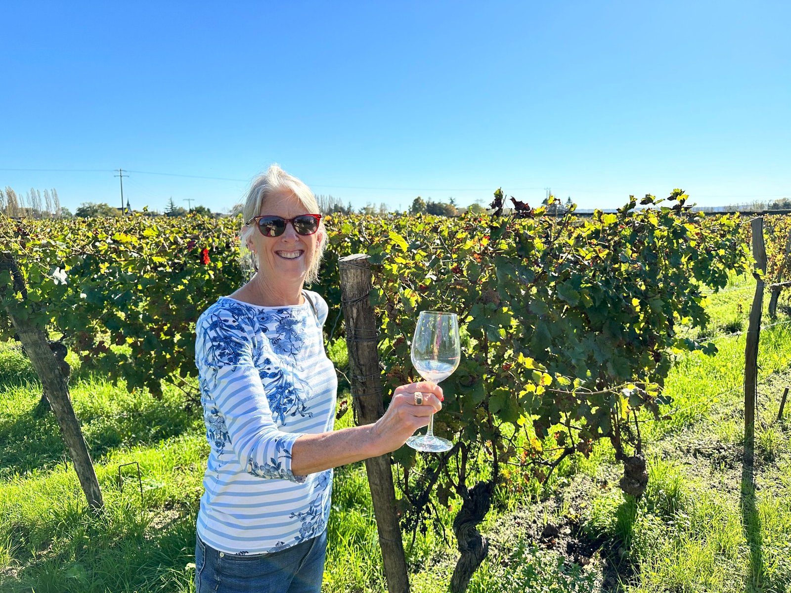 Susan Richards of Always Sharing Wine holding a glass in a vineyard and smiling