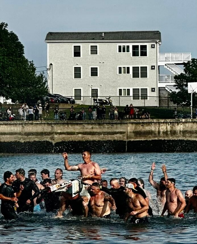 The 2026 winner of the Greasy Pole with the flag being carried off beach by fellow competitors